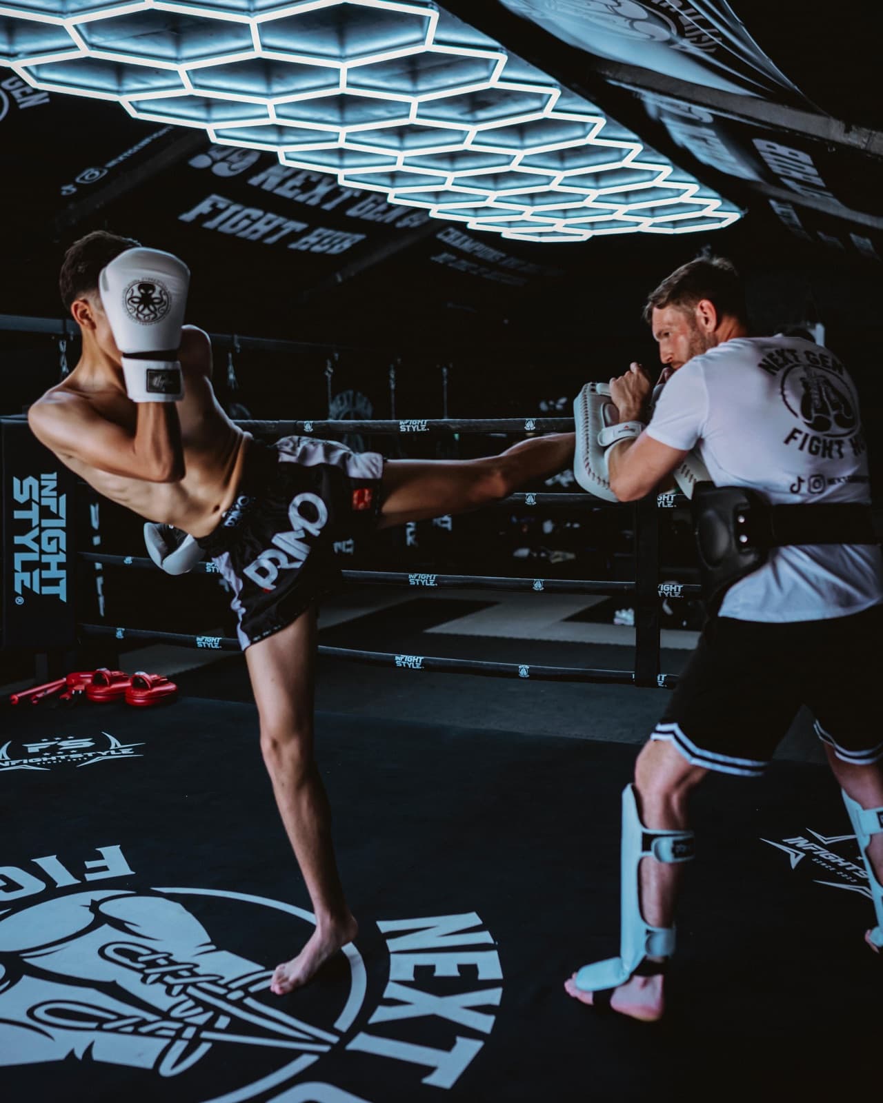 Hayden holding pads for a high kick under the lights at NextGen Fight Hub